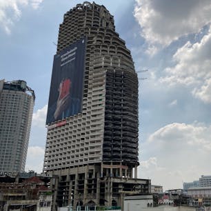 サトーンユニークタワー
バンコクのサパーンタクシン駅から見える有名な廃墟ビル。
49階建てのビルだが、20年以上前から建設工事がストップしているらしい。
巨大看板だけは現役なので、看板を付け替える人は登っているのだろう。
今は一般の人は入れないらしい。